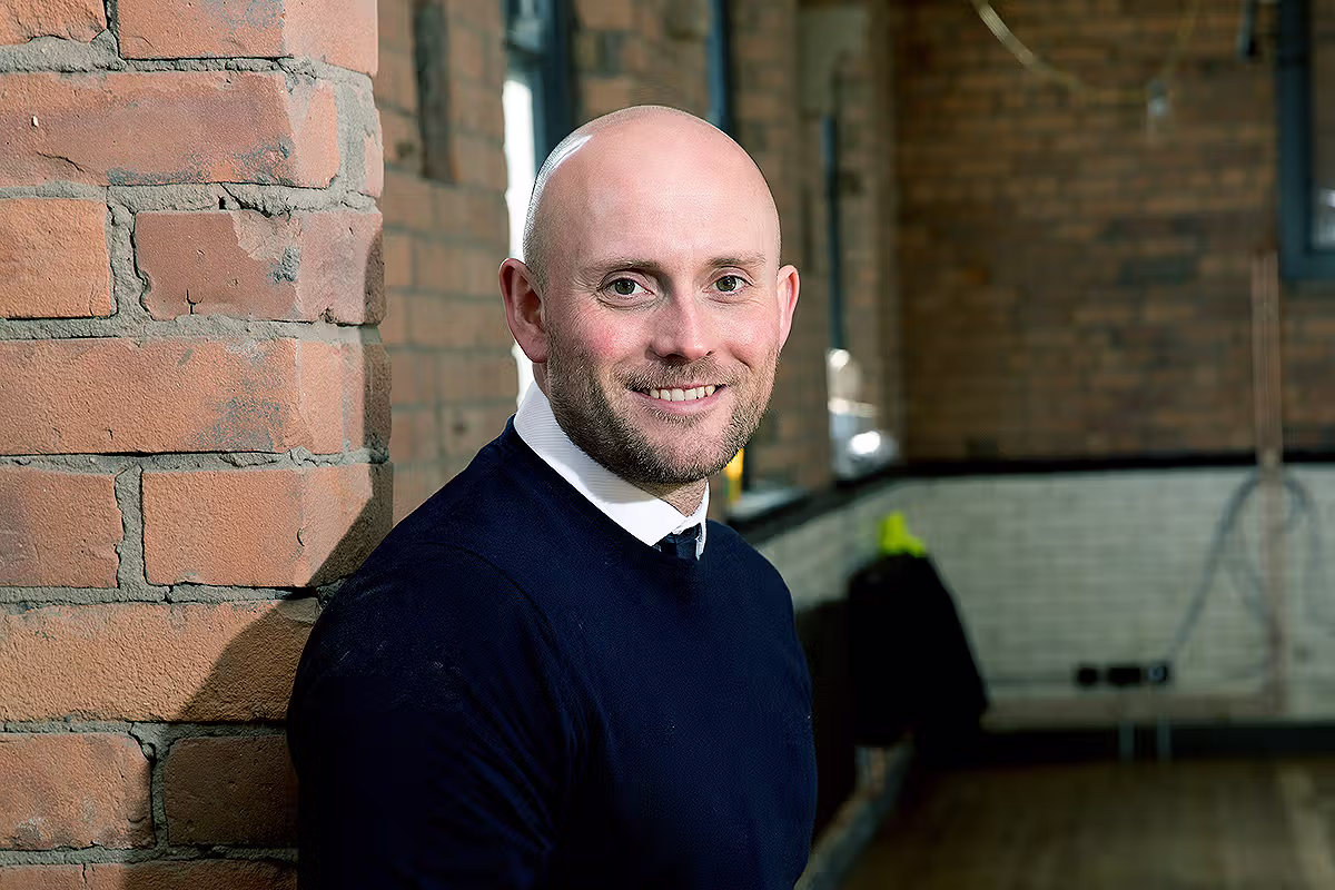 Office environmental portrait of a business professional beside a brick workspace wall