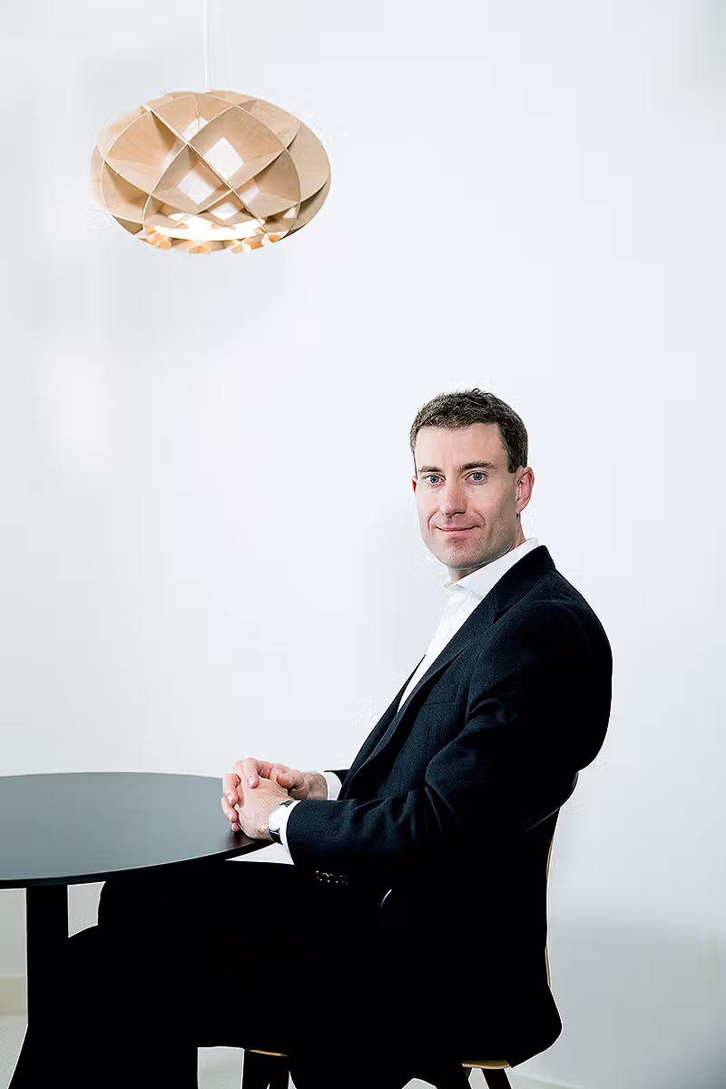 Executive portrait of a businessman seated at a high table in a white office interior