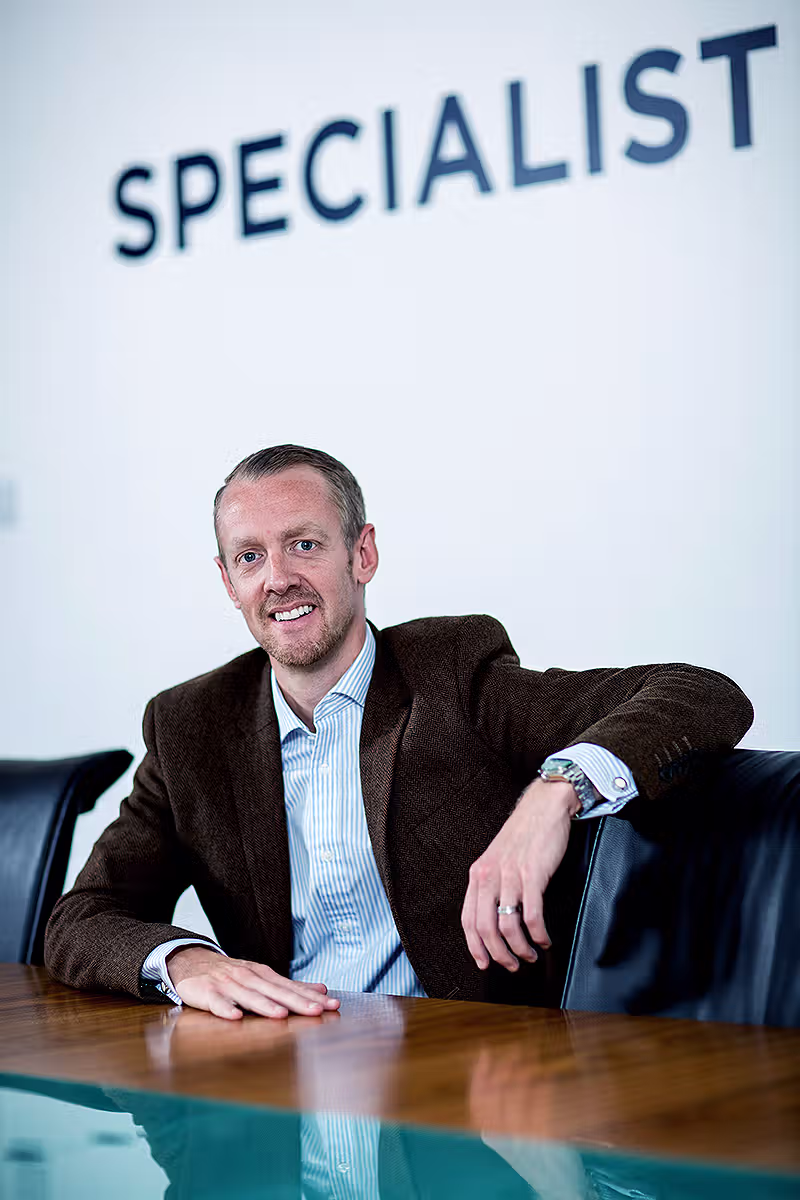 Executive portrait of a man seated beside Specialist branding in an office