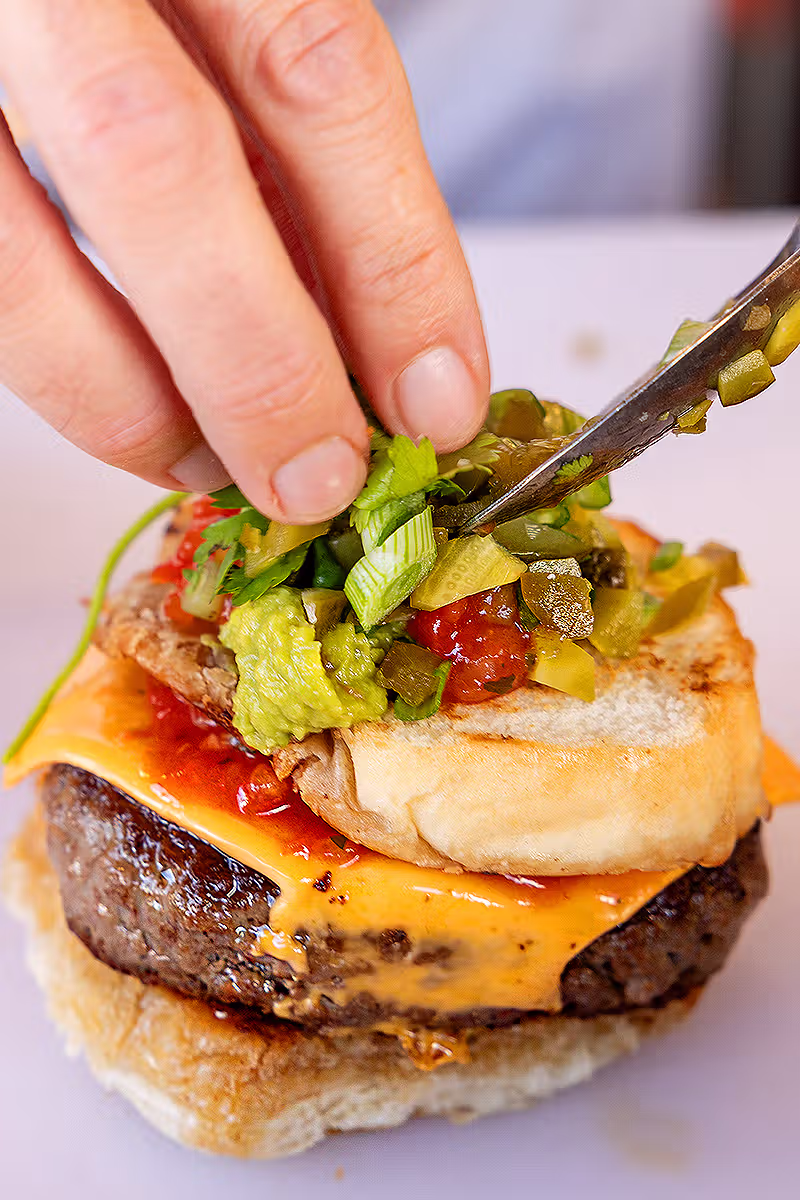 Food PR photography in London showing a close-up burger being dressed with pickles and garnish during the Co-op Food Festival
