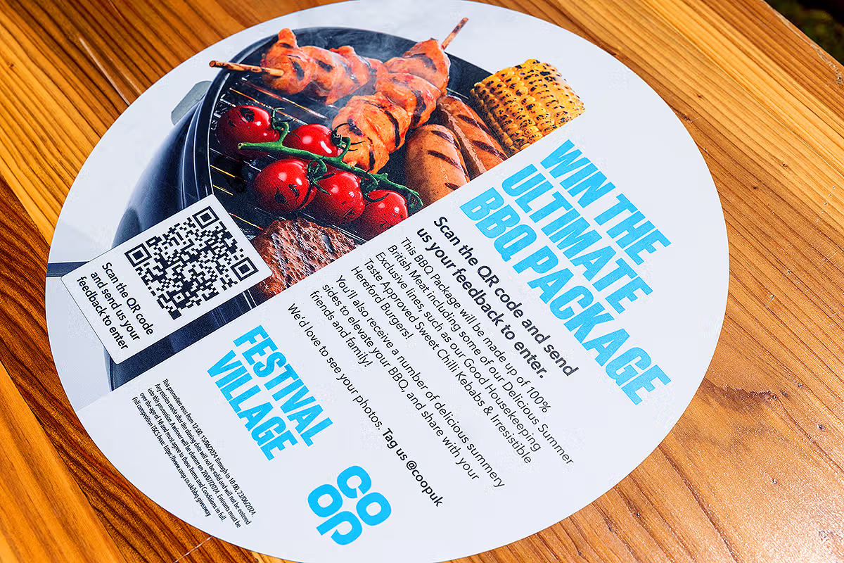 Co-op Food Festival campaign detail showing Ultimate BBQ Package QR code leaflet on a table at the London activation